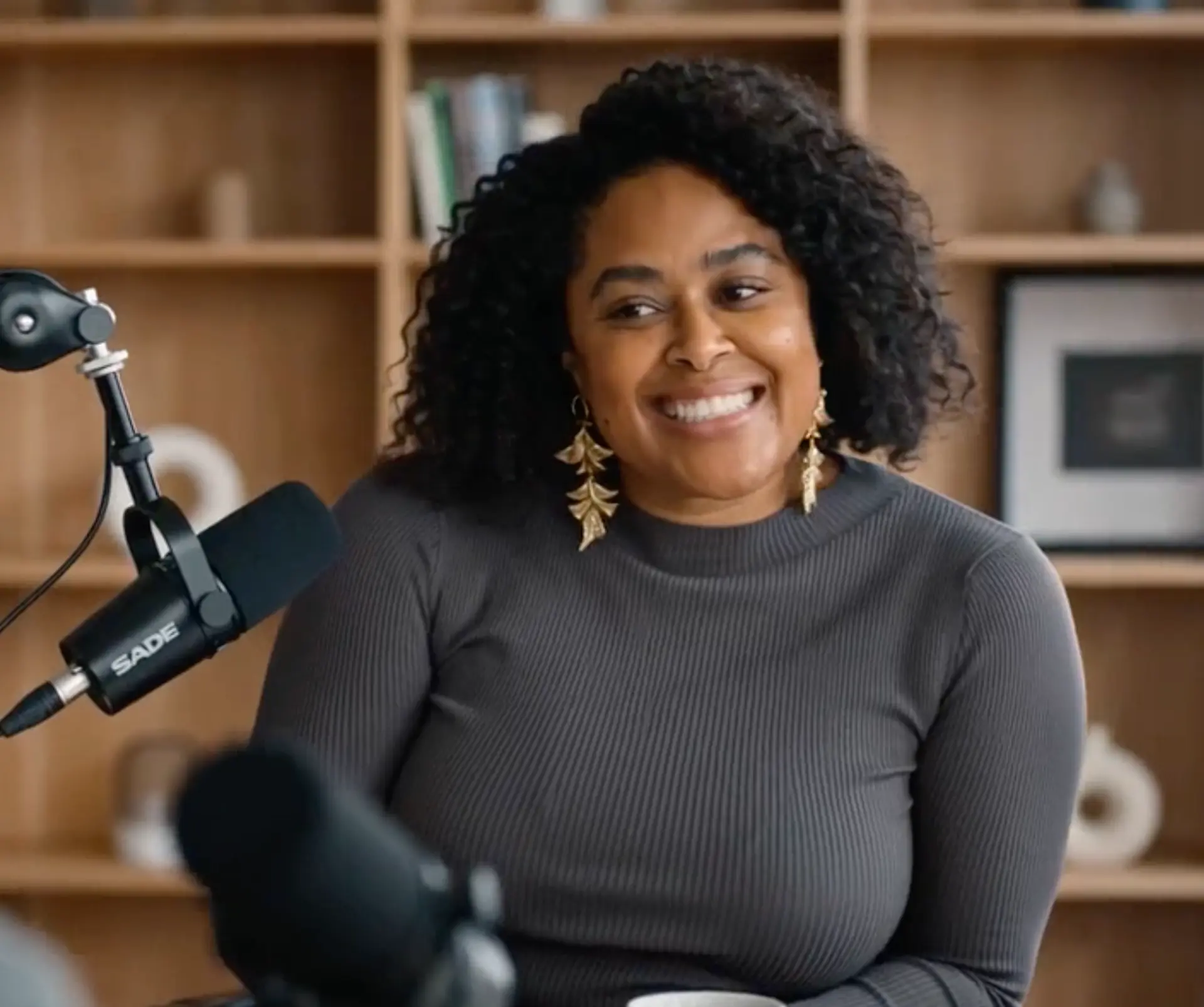 Colet Williams in the podcast studio, wearing gold leaf earrings and a mock-neck sweater